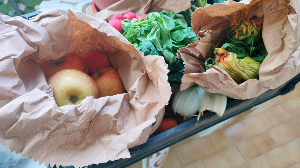 cesto di frutta e verdura misto proveniente dall'alveare di Alessandria. Nella foto si riconoscono mele, zucchine, rapanelli all'interno dei loro sacchetti di carta all'interno di una box.